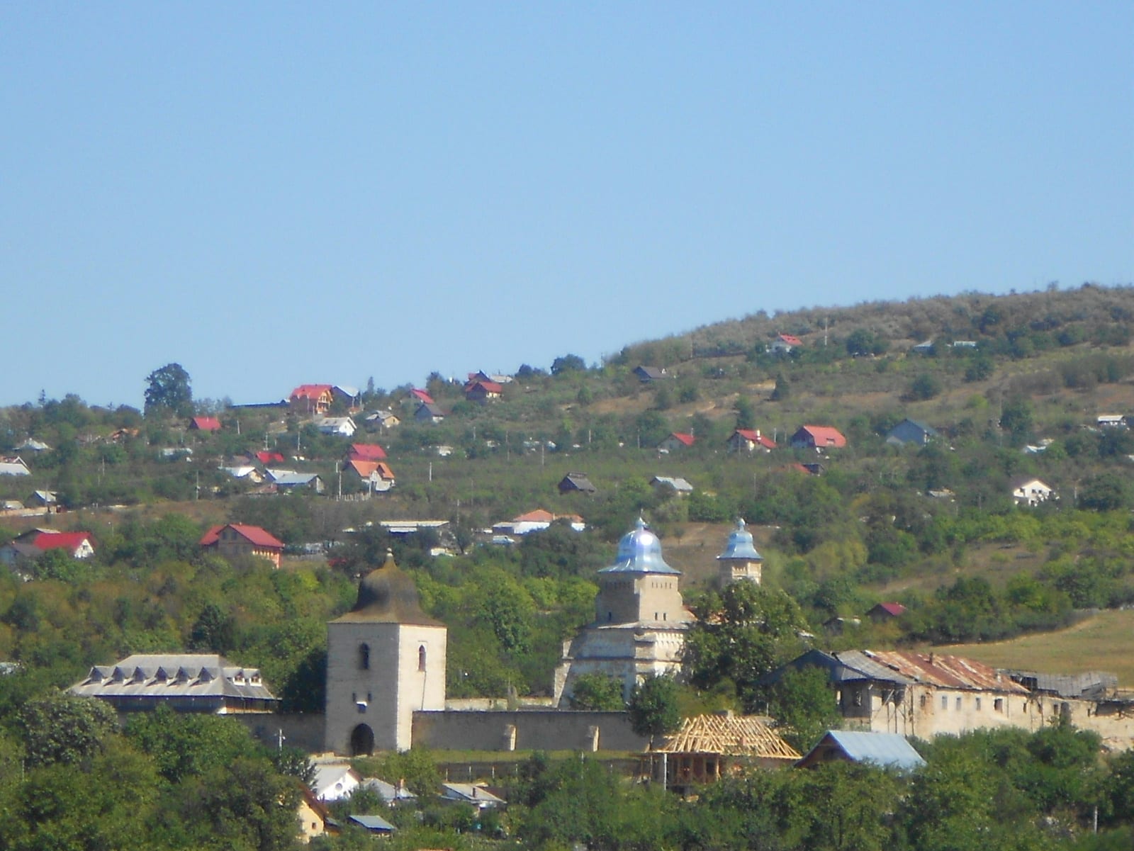 Ansamblul Mănăstirii Bârnova pe deal deasupra satului: turnul-clopotniță de piatră, biserica cu turle albastre și zidul de incintă