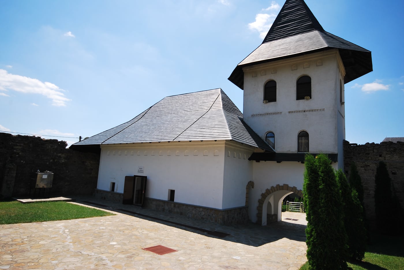 Turnul-clopotniță de intrare al Mănăstirii Hadâmbu, cu poartă boltită și ziduri albe de incintă — arhitectura de cetate moldovenească ridicată în secolul al XVII-lea împotriva incursiunilor tătare