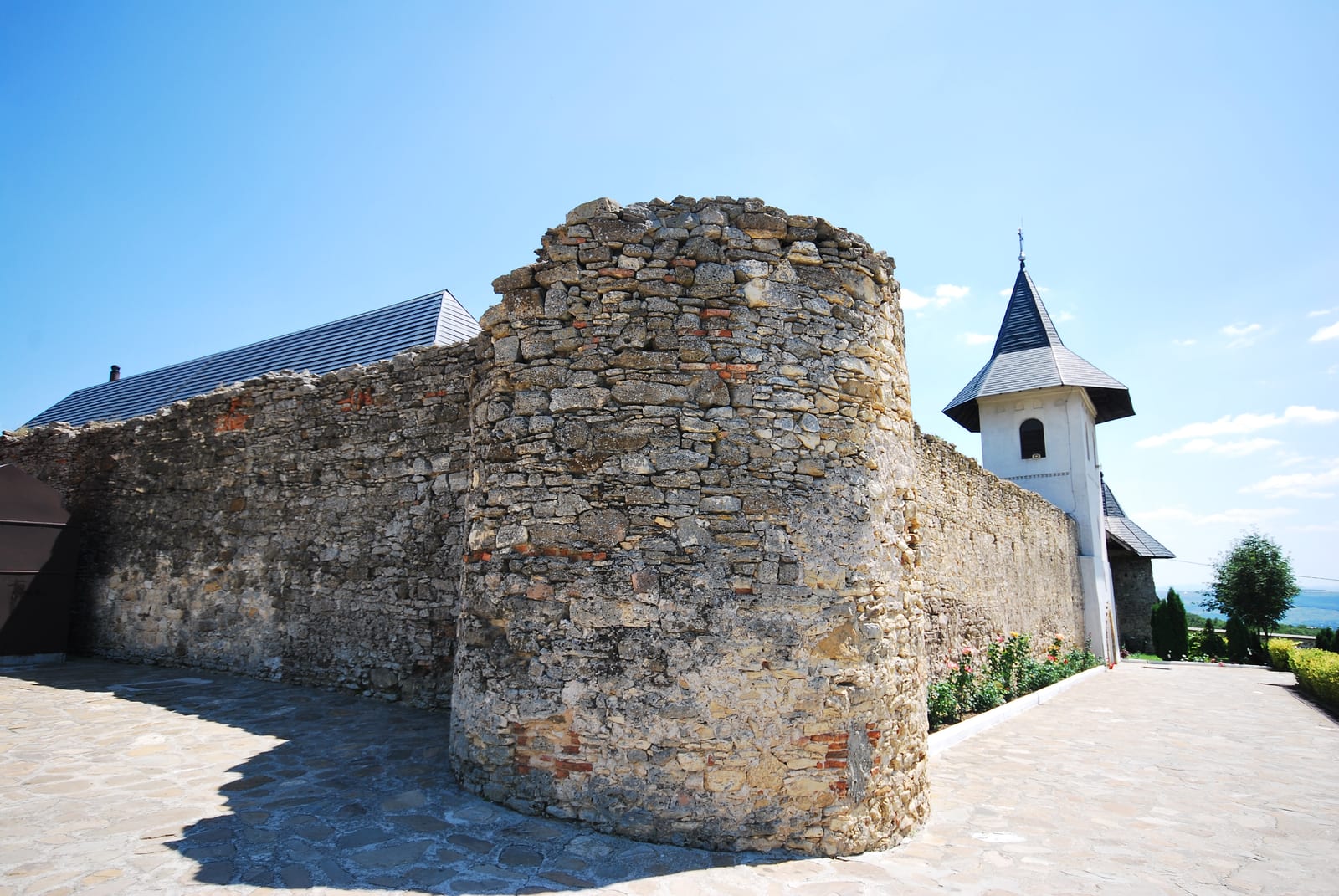 Zidul de incintă din piatră și turnul rotund de colț al Mănăstirii Hadâmbu, sub cer senin