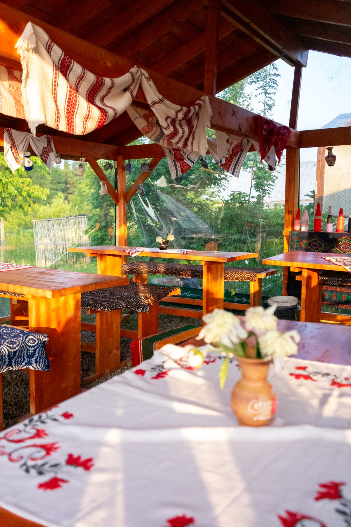 Mesele din foișorul de la Căsuța cu Maci la ora cinei, cu fețe de masă brodate și lumină aurie, locul unde se servesc sarmalele de la ceaun