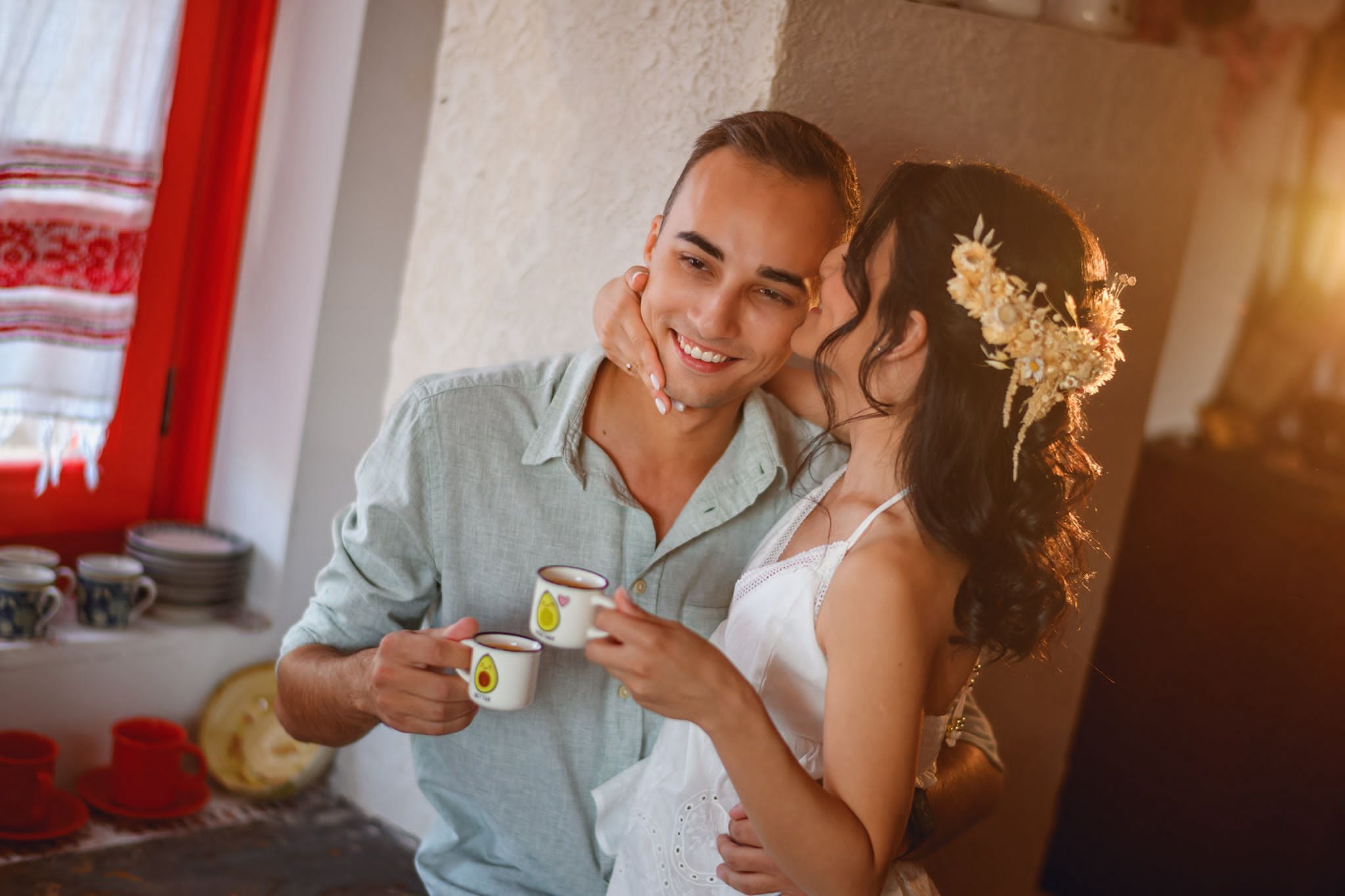 Mirii cu cafeaua în mână în bucătăria cu fereastră roșie și ștergar țesut, în dimineața nunții
